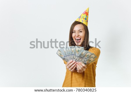 Beautiful caucasian lucky young happy woman in yellow clothes, birthday party hat holding wad of cash money, celebrating holiday on white background isolated for advertisement. Winner with dollars