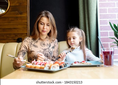 Beautiful Caucasian Mom And Daughter Eating Rolls And Sushi At Family Lunch In A Japanese Restaurant
