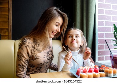 Beautiful Caucasian Mom And Daughter Eating Rolls And Sushi At Family Lunch In A Japanese Restaurant
