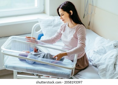 Beautiful Caucasian Mother Calm Down Her Newborn Baby Sleeping On Hospital Bed In Postpartum Ward. Healthcare And Medical Parent Love Lifestyle Nursery Mothers Day Concept.