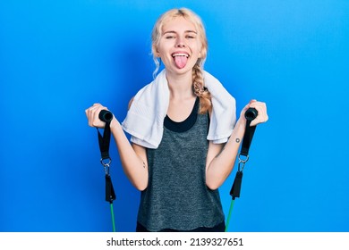 Beautiful caucasian sports woman with blond hair training arm resistance with elastic arm bands sticking tongue out happy with funny expression. 