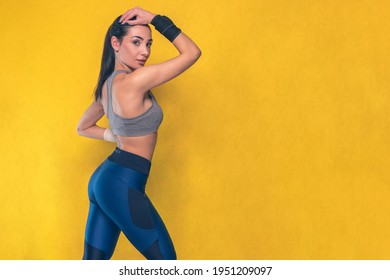 Beautiful caucasian sports woman in blue leotard and blue leggings sportswear - Studio shooting with pretty slim young brunette athletic model girl posing during gymnastics workout showing her side