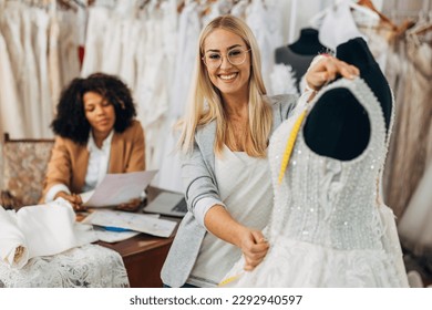 A beautiful caucasian tailor measures upper part of a wedding dress - Shutterstock ID 2292940597