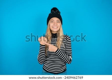 beautiful caucasian teen girl knitted  hat and striped T-shirt In hurry pointing to wrist watch, impatience, looking at the camera with relaxed expression