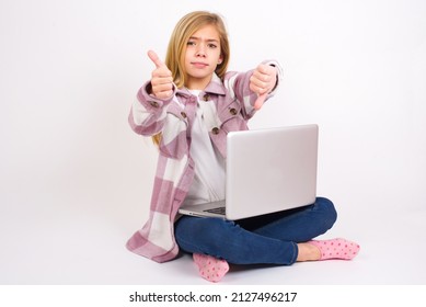 Beautiful Caucasian Teen Girl Sitting With Laptop In Lotus Position On White Background Feeling Unsure Making Good Bad Sign. Displeased And Unimpressed.