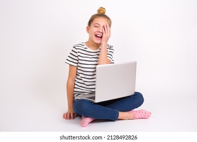 Beautiful Caucasian Teen Girl Sitting With Laptop In Lotus Position On White Background Makes Face Palm And Smiles Broadly, Giggles Positively Hears Funny Joke Poses