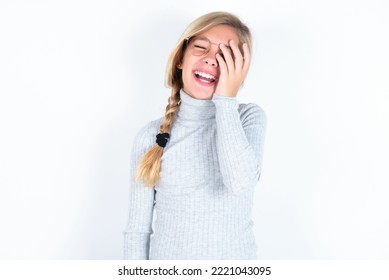 Beautiful Caucasian Teen Girl Wearing Gray Turtleneck Sweater Over White Wall Makes Face Palm And Smiles Broadly, Giggles Positively Hears Funny Joke Poses