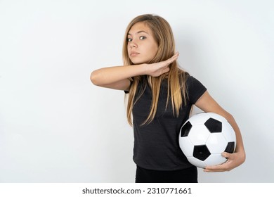beautiful caucasian teen girl wearing sportswear holding a football ball over white wall cutting throat with hand as knife, threaten aggression with furious violence. - Shutterstock ID 2310771661