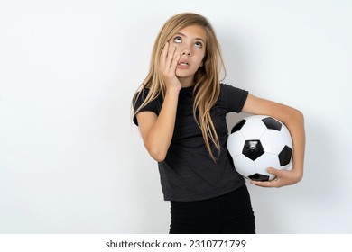 beautiful caucasian teen girl wearing sportswear holding a football ball over white wall keeps hands on cheeks has bored displeased expression. Stressed hopeless model - Shutterstock ID 2310771799