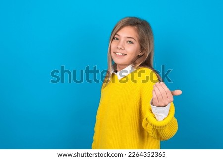beautiful caucasian teen girl wearing yellow sweater over blue wall inviting to come with hand. Happy that you came