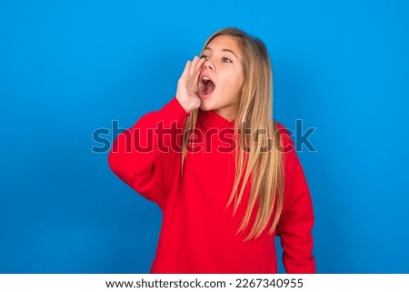 Beautiful caucasian teen girl wearing red sweatshirt over blue background profile view, looking happy and excited, shouting and calling to copy space.