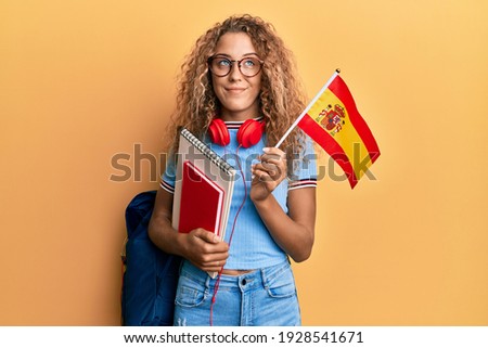 Beautiful caucasian teenager girl exchange student holding spanish flag smiling looking to the side and staring away thinking. 