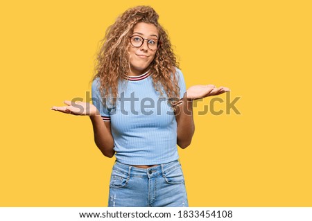 Beautiful caucasian teenager girl wearing casual clothes and glasses clueless and confused expression with arms and hands raised. doubt concept. 