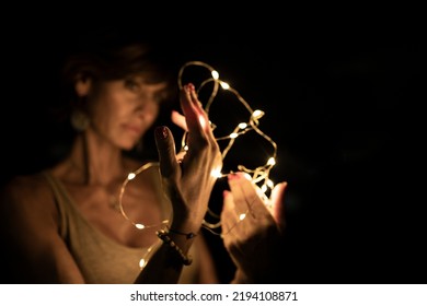 Beautiful caucasian woman, blurred face, holding string lights in the dark. Copy space. Holidays or magic background or wallpaper.