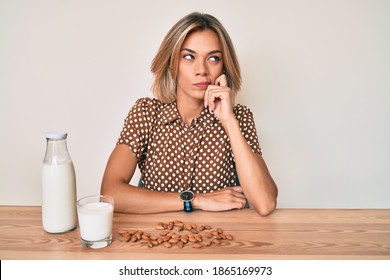 Beautiful Caucasian Woman Drinking Healthy Almond Milk Thinking Concentrated About Doubt With Finger On Chin And Looking Up Wondering 