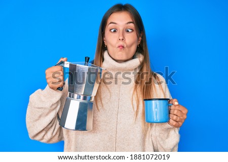 Beautiful caucasian woman drinking italian coffee making fish face with mouth and squinting eyes, crazy and comical. 