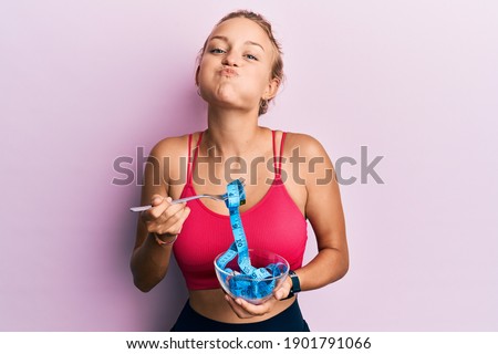 Beautiful caucasian woman eating measure meter doing diet for weight loss puffing cheeks with funny face. mouth inflated with air, catching air. 