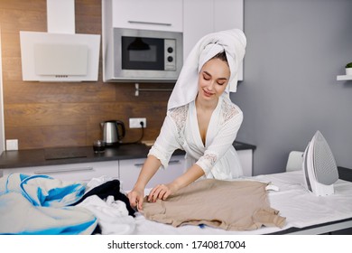 Beautiful Caucasian Woman Enjoy Ironing Clothes At Home, She Is Preparing To Go Outside, Stand Using Modern Iron, Wearing Bathrobe And Towel After Bath