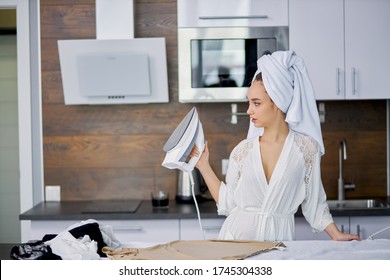 Beautiful Caucasian Woman Enjoy Ironing Clothes At Home, She Is Preparing To Go Outside, Stand Using Modern Iron, Wearing Bathrobe And Towel After Bath