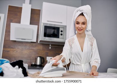 Beautiful Caucasian Woman Enjoy Ironing Clothes At Home, She Is Preparing To Go Outside, Stand Using Modern Iron, Wearing Bathrobe And Towel After Bath