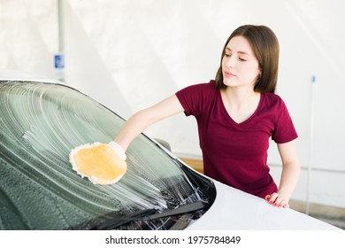 Beautiful caucasian woman in her 20s with cleaning mitts washing the windshield of her car at home or a self service car wash  - Shutterstock ID 1975784849