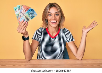 Beautiful caucasian woman holding australian dollars celebrating achievement with happy smile and winner expression with raised hand 