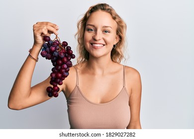 Beautiful caucasian woman holding branch of fresh grapes looking positive and happy standing and smiling with a confident smile showing teeth 