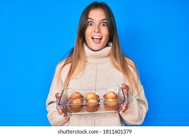 Beautiful caucasian woman holding homemade muffins celebrating crazy and amazed for success with open eyes screaming excited. 
