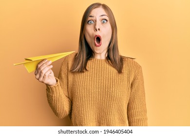 Beautiful Caucasian Woman Holding Paper Airplane Scared And Amazed With Open Mouth For Surprise, Disbelief Face 