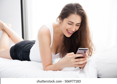 Beautiful Caucasian Woman Laying Down On White Bed Using Mobile Phone And Smile