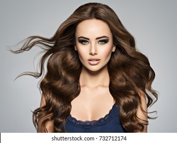 Beautiful Caucasian Woman With Long Brown Curly Hair. Portrait Of A Pretty Young Adult Girl. Sexy Face Of An Attractive  Lady Posing At Studio Over Grey Background.