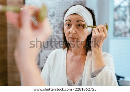 Beautiful caucasian woman massaging with jade stone roller in bathroom.