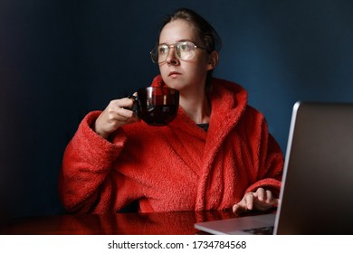Beautiful Caucasian Woman In Red Dressing Gown And Eyeglasses Hold Cup Of Tea When Working On The Notebook Over Blue Background