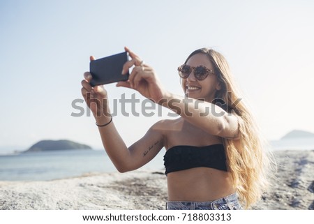 Beautiful Caucasian woman taking photo by the sea with her mobile phone camera.