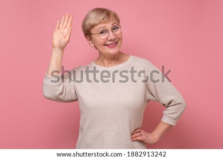 Beautiful caucasian woman waiving saying hello happy and smiling, friendly welcome gesture. Studio shot on pink wall.