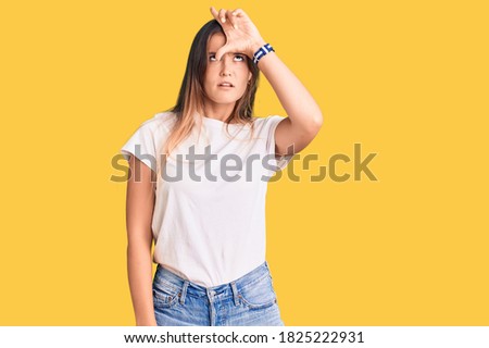 Beautiful caucasian woman wearing casual white tshirt making fun of people with fingers on forehead doing loser gesture mocking and insulting. 