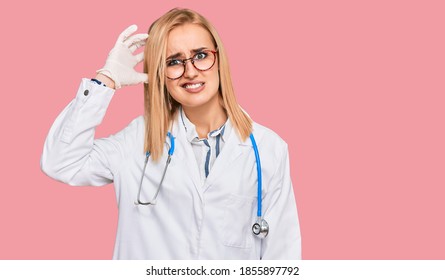 Beautiful Caucasian Woman Wearing Doctor Uniform And Stethoscope Confuse And Wonder About Question. Uncertain With Doubt, Thinking With Hand On Head. Pensive Concept. 