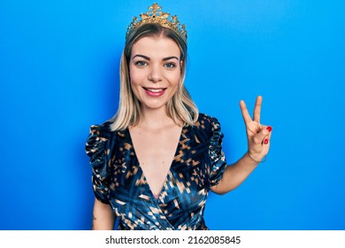 Beautiful Caucasian Woman Wearing Princess Crown Smiling With Happy Face Winking At The Camera Doing Victory Sign. Number Two. 