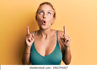 Beautiful Caucasian Woman Wearing Sleeveless Shirt Over Yellow Background Amazed And Surprised Looking Up And Pointing With Fingers And Raised Arms. 