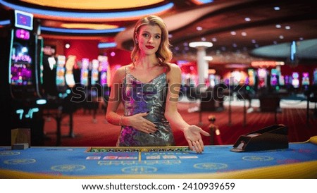Beautiful Caucasian Woman Working As A Dealer At Classy Casino. Professional Female Baccarat Croupier In a Fancy Silver Dress, Presenting Playing Cards, Looking At Camera And Smiling