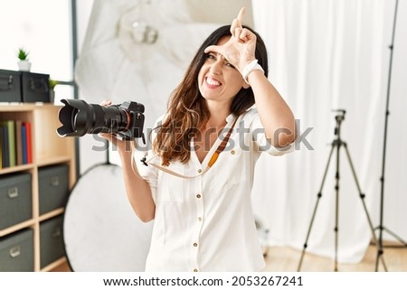 Beautiful caucasian woman working as photographer at photography studio making fun of people with fingers on forehead doing loser gesture mocking and insulting. 