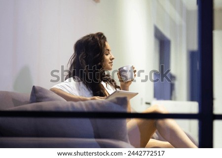 Beautiful Caucasian young relaxed woman in robe resting on sofa in living room drinking coffee holding cup in hands. Attractive pretty female indoors. spying through the glass Stock fotó © 