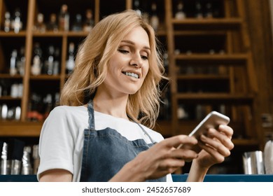 Beautiful caucasian young waitress bartender barista small business owner using smart phone for takeout food delivery online at the bar counter - Powered by Shutterstock