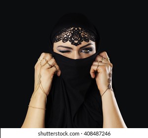 Beautiful caucasian young woman with black veil on face, one eye closed, fancy arabian costume. Isolated on black