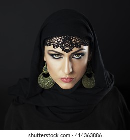 Beautiful Caucasian young woman with black fancy Arabian costume and ornamental jewelry on black background