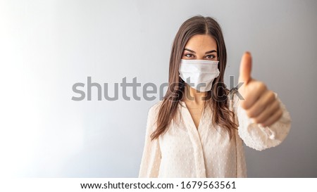 Beautiful caucasian young woman with disposable face mask. Protection versus viruses and infection. Studio portrait, concept with white background. Woman showing thumb up. 