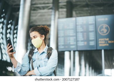 Beautiful Caucasian Young Woman Wearing Face Mask In The Airport Using Mobile App To Check Flight Timetable. Covid Passport And Safe Travel In 2022