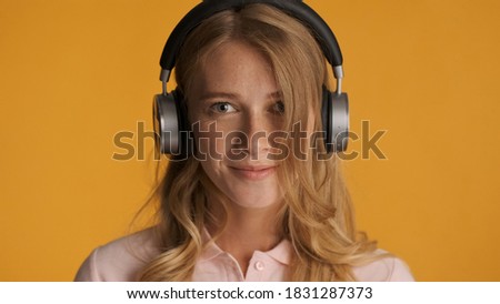 Beautiful charming blond girl in headphones dreamily looking in camera over colorful background