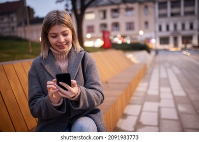 Beautiful charming girl in coat standing in street and looking at telephone.Nice winter day. - Shutterstock ID 2091983773