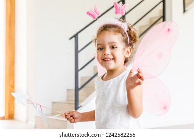 Beautiful charming little girl wearing fairy costume with magic wand, in a modern house interior, with white background and brown wood floor. Natural light. Horizontal framing. - Powered by Shutterstock